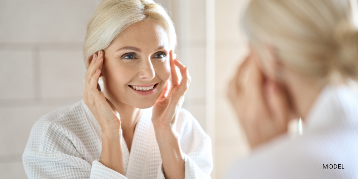 middle aged woman looking at her reflection in the mirror after having a facelift in fort worth at dfw plastic surgery